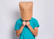 © DenisNata - Portrait of teen boy with paper bag over head. Teenager cover head with bag holding hand near face posing in studio. Child pulling paper bag over head.