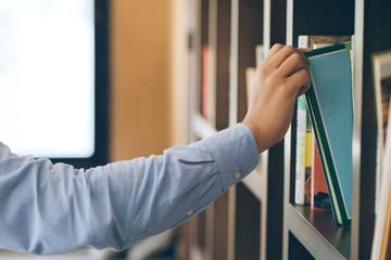 Hand of student selecting a book from book shelf in library room background, people, learning, education and school concept