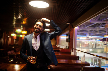 Wall Mural - Handsome well-dressed arabian man with glass of whiskey and cigar posed at pub.