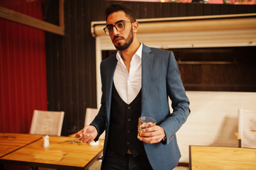 Wall Mural - Handsome well-dressed arabian man smoke cigar with glass of whiskey at balcony of pub.