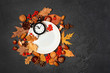 empty white plate and clock alarm, autumn leaves, nuts, cones, acorns, berries on dark table. Autumn harvest season, Halloween and thanksgiving day table setting. Fall time. mock up