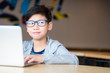 © myboys.me - Smart looking Asian preteen boy with eye blue light blocking glasses rolling eyes smiling happily, using computer laptop to study online lessons. Online learning and self study concept.