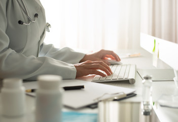 Hands of a doctor working on a computer at a table in a clinic.