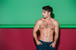 sexy shirtless man in denim jeans holding hands in pockets and looking away on green and red background