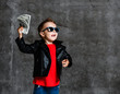 Looking up rich kid boy in sunglasses, leather jacket and red t-shirt holding a bundle of dollars going to throw it up