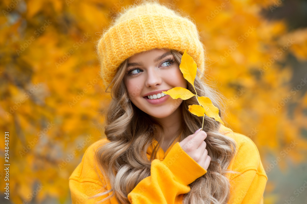 Beautiful girl walking outdoors in autumn. Smiling girl collects yellow leaves in autumn. Young woman enjoying autumn weather. - obrazy, fototapety, plakaty 