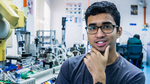 Fotomural A young Malay engineering student with spectacles working in the lab and thinking by holding chin
