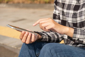 Woman hand holding and using mobile phone sitting in the outdoor