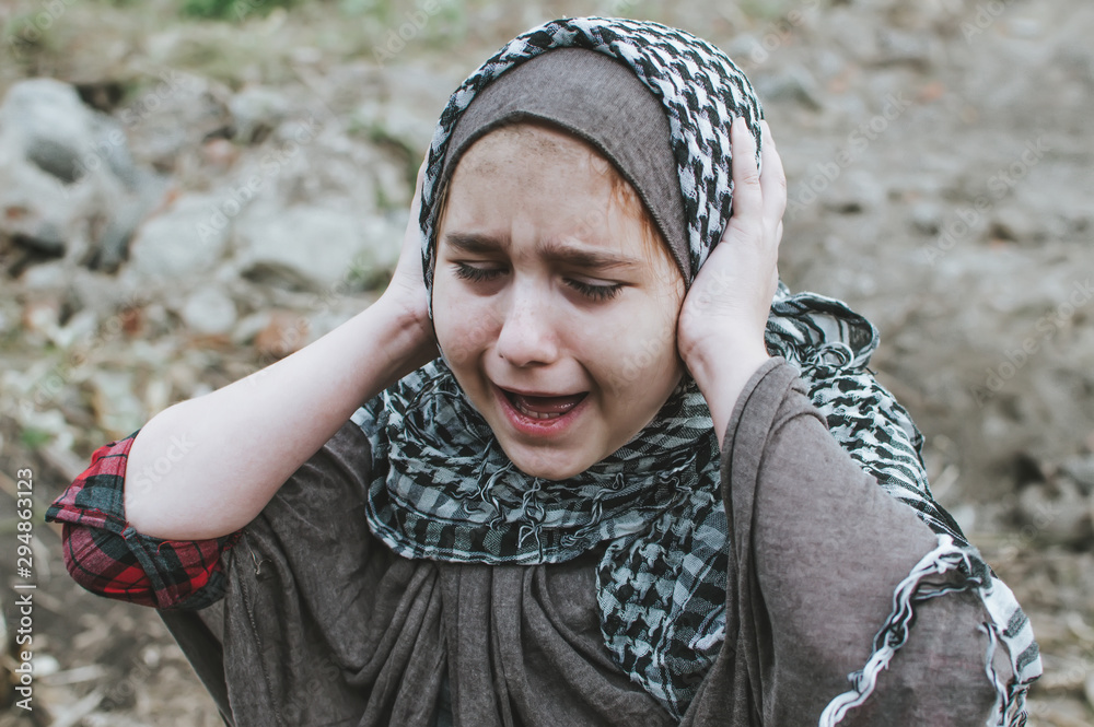a refugee child in the war, a Muslim girl with a dirty face on the ruins, the concept of peace and war, the child is crying and waiting for help. - obrazy, fototapety, plakaty 