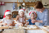 Fototapeta  - Family is cooking Christmas cookies together in cozy home kitchen for holiday dinner. Funny kids and woman bake Xmas biscuits. Mother is teaching daughters. Lifestyle moment. Children chef concept.
