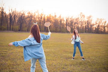 Two young women play badminton outdoors at sunset. Best friends