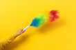 Colorful feather duster in hand on yellow background. Cleaning concept.
