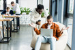© LIGHTFIELD STUDIOS - african american businessman holding coffee to go while standing near colleague using laptop and showing shrug gesture