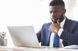© Prostock-studio - Pensive african american young man working with laptop in office