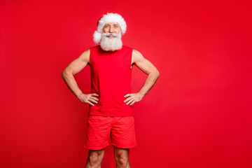 Poster - Portrait of cheerful santa claus cap putting his hands on waist true coach wearing sports wear isolated over red background