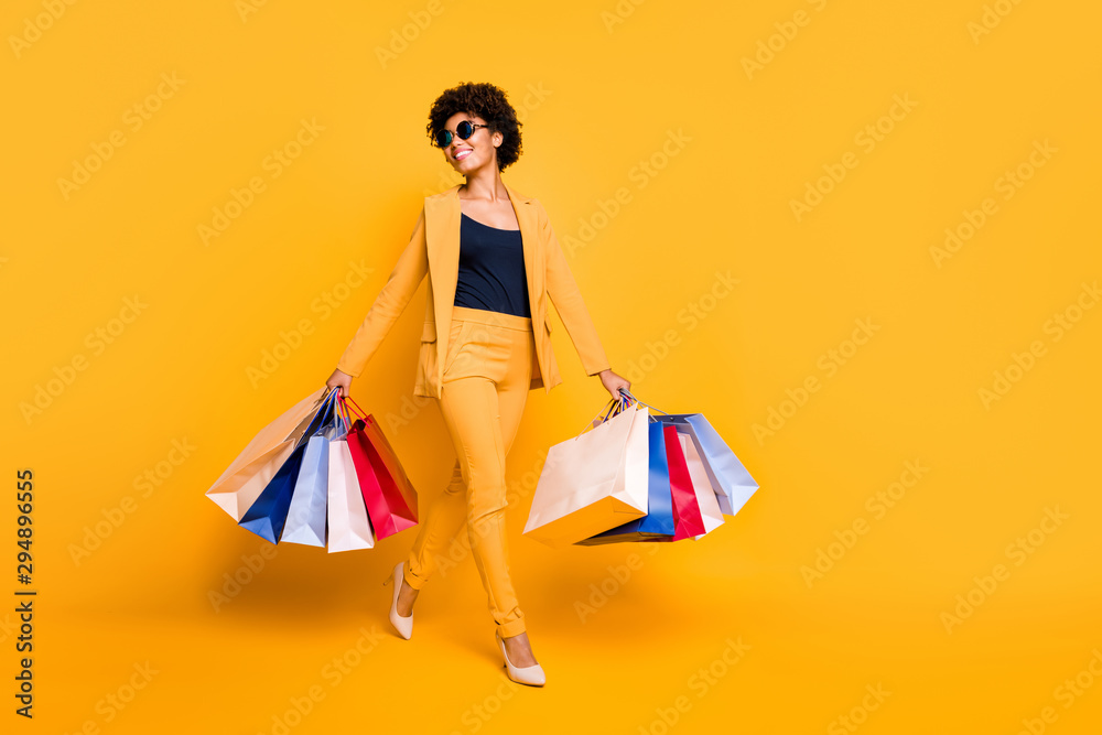 Full size photo of positive cheerful girl have leisure time feel dream dreamy hold bags go from shopping center wear style blazer trousers stilettos isolated over yellow color background - obrazy, fototapety, plakaty 