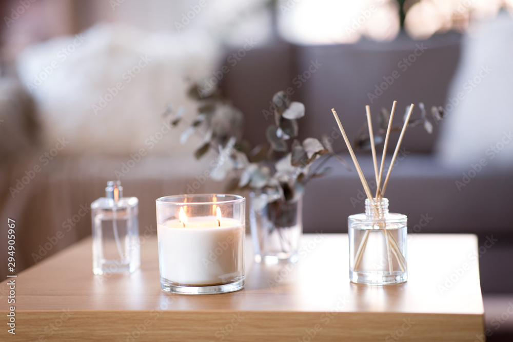 decoration, hygge and aromatherapy concept - aroma reed diffuser, burning candle, branches of eucalyptus populus and perfume on table at home - obrazy, fototapety, plakaty 