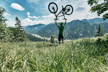 Mountain Biker In The Mountains Holding Up His Mountain Bike, Bavaria, Germany