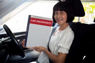 Happy Asian senior woman holding car insurance document book and sitting in car, Safety vehicle and protection client person concept