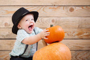 baby in black hat with pumpkins on wooden background