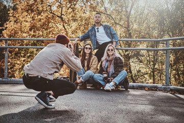 Wall Mural - Young man in hat is making a photo of his friends at sunny autumn park.