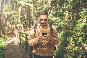 Modern hipster guy holding mobile phone in nature. Travel, technology and healthy lifestyle concept.