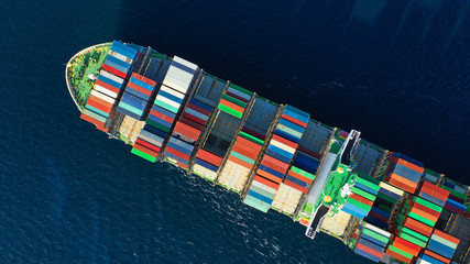 Aerial top down photo of Container cargo Ship carrying load in truck-size colourful containers in deep blue open ocean sea 