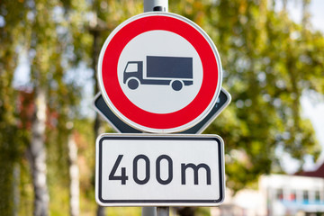 A round red white road sign in Germany. For trucks the entrance is prohibited in 400 meters. A green tree with soft bokeh in the background.