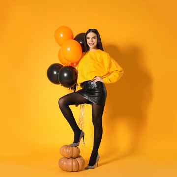 Beautiful woman with balloons and pumpkins on yellow background. Halloween party