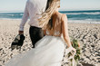 © Westend61 - Rear view of bride and groom walking on the beach