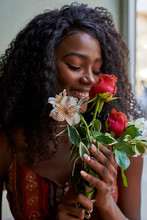 Portrait Of Young African Woman Smelling Flowers And Smiling In A Cafe