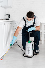 Wall Mural - exterminator in protective mask holding toxic spray near kitchen cabinet