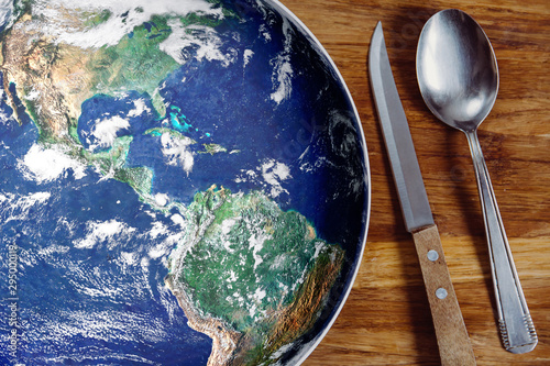 The planet Earth plate with a fork and knife on a wooden background. World hunger concept. Feed the world.