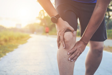 Injury from workout concept : Asian man use hands hold on his knee while running on road in the park. Shot in morning time, sunlight and warm effect with copy space for text or design