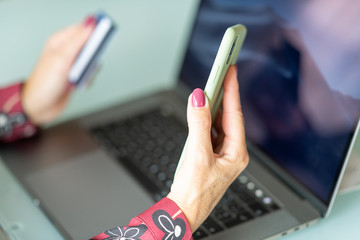 Poster - Woman doing online shopping at home. Detail on hands holding smartphone and credit card and modern laptop keyboard on background