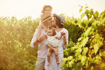 Young family with children having fun in nature on summer sunset background. Mother and father hugs his two little daughters 