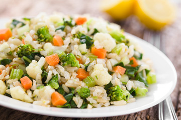Wall Mural - Fresh cooked brown rice with steamed vegetables (broccoli, cauliflower, swiss chard, carrot, celery) on plate, lemon in the back (Selective Focus, Focus one third into the plate)