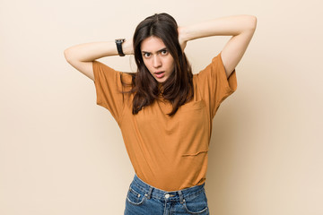 Wall Mural - Young brunette woman against a beige background covering ears with hands trying not to hear too loud sound.