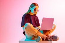 Modern Girl With Laptop, Tablet Computer. Free Creativity. A Young Blogger Makes A Home Office. Colored Neon Light And Background.