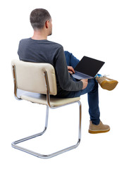 Canvas Print - Back view of a man who sits on a chair with a laptop.