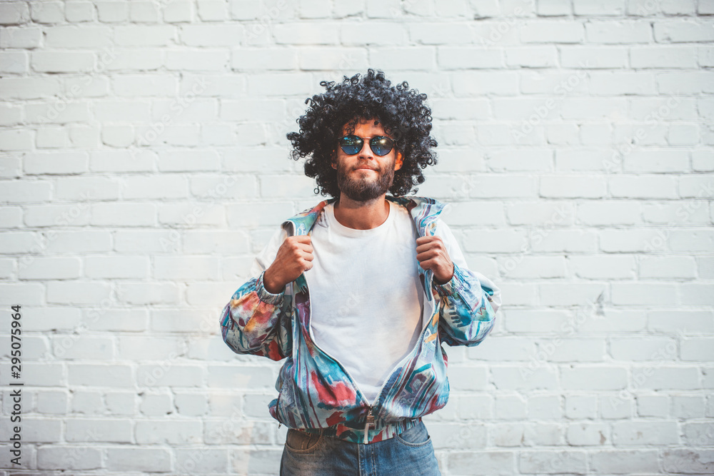 Stylish young man in a retro jacket. Fashion trends of 90s. Handsome hipster guy with beard with curly hair. - obrazy, fototapety, plakaty 