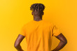 © Asier - Young black man wearing rastas over yellow background from behind, looking back.