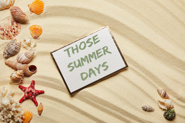 top view of card with those summer days lettering near seashells, red starfish and corals on sandy beach