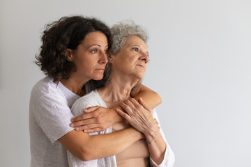 Pensive adult daughter hugging senior mother and looking away. Middle aged woman embracing elderly lady. Daughter affection concept