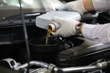 Focus on auto mechanic in gloves replacing and pouring fresh oil into engine at automobile service station. Vehicle inspection concept. Blurred background