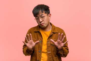 Young chinese man wearing a jacket rejecting something doing a gesture of disgust