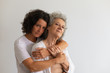 © Mangostar - Serious adult daughter and senior mother posing in studio. Middle aged woman hugging elderly lady and looking at camera. Mother and daughter portrait concept