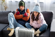 attractive girlfriend and boyfriend in winter outfit warming up near heater