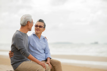 Wall Mural - Happy asian senior couple  have fun and enjoy at the beach, senior man and woman hugging while sitting on the beach Retirement Lifestyle Healthy  Travel Vacation Concept