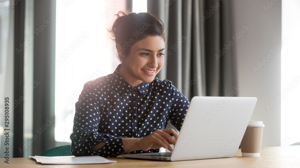 Happy young indian businesswoman using computer sit at office desk - obrazy, fototapety, plakaty 